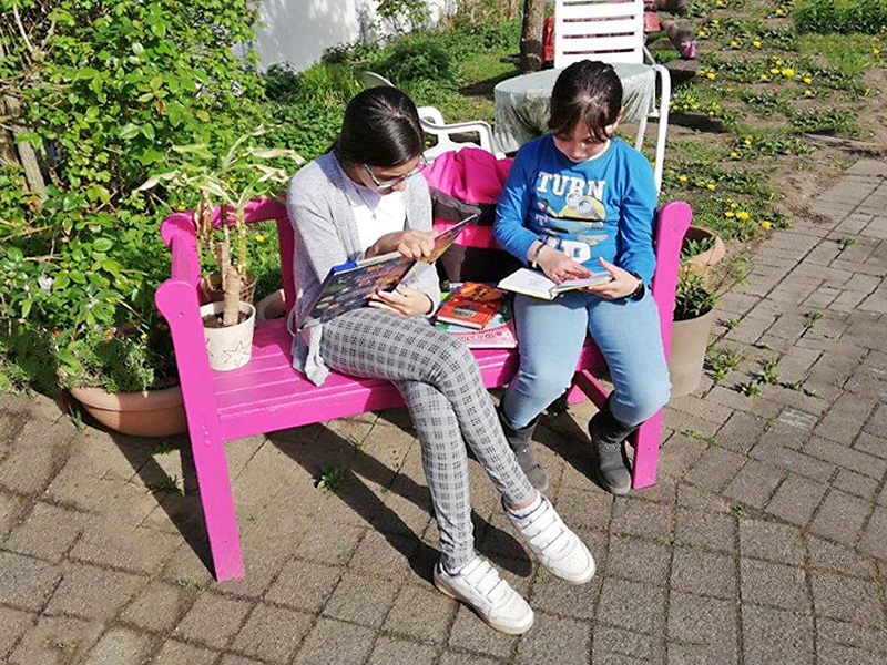 Zwei Mädchen lesen Bücher auf einer Bank vor dem Schulgebäude