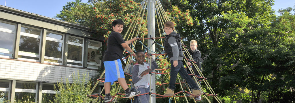 4 Jungen auf dem Schulhof auf einem Klettergerät mit Netz